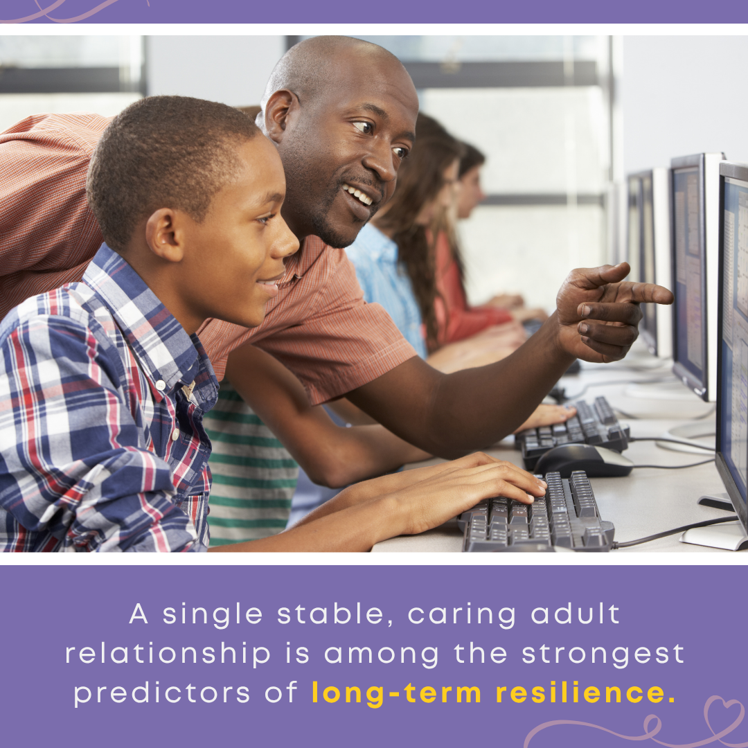 A teacher points to a computer screen while guiding a young student, showing how can teachers help students, including a child in foster care, build long-term resilience through a stable relationship.