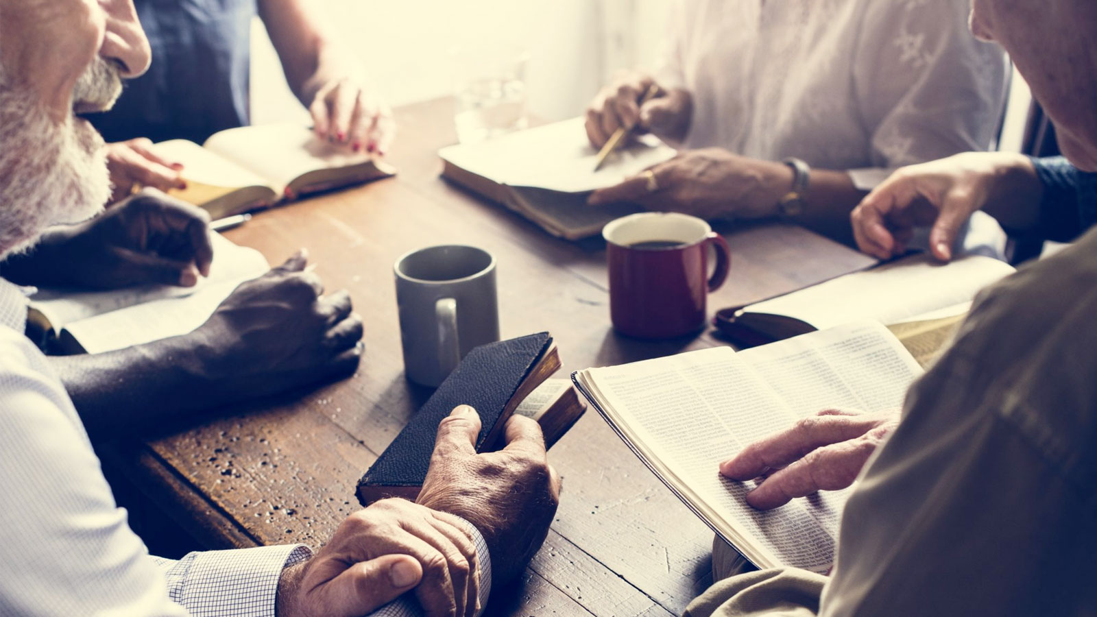 A group discussion around a table with Bibles and coffee mugs