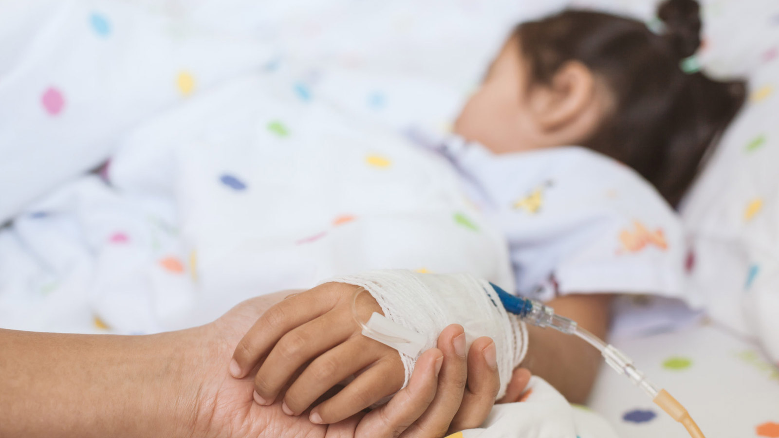 Hospital sitter holds the hand of a foster child during their hospital stay.
